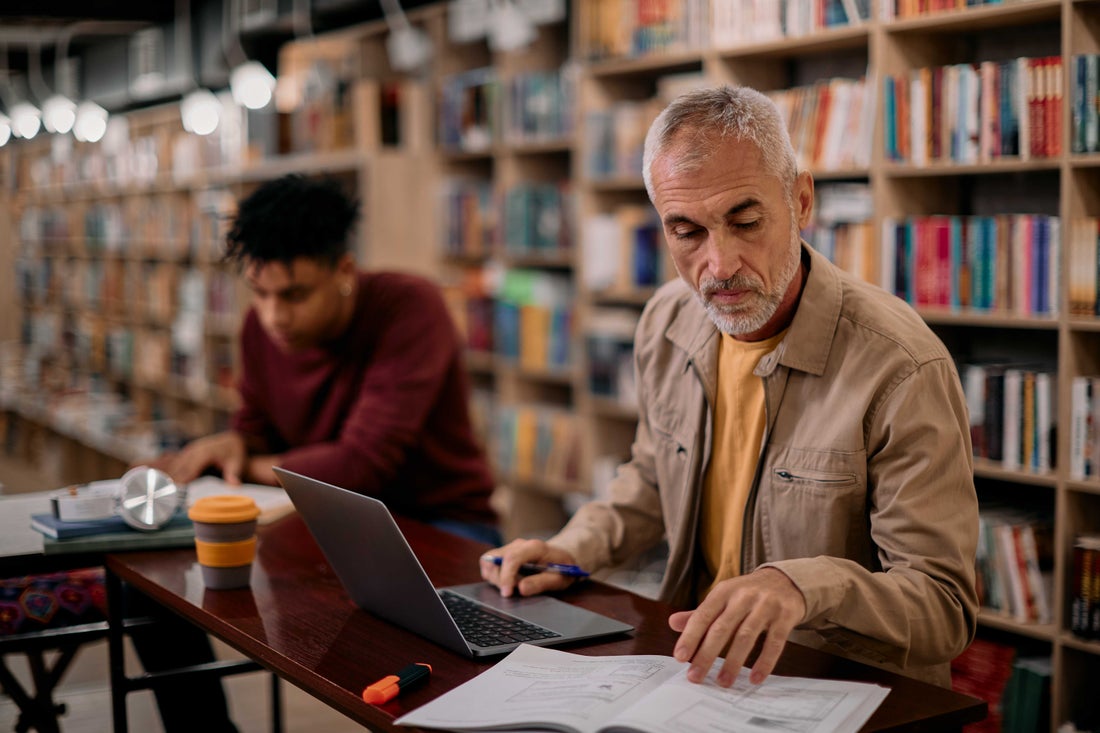 man sitting at laptop reading papers.