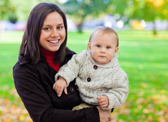 A woman wearing a black jacket holding her baby wearing a white sweater
