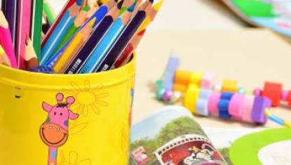 Colored pencils in a yellow tin with a book to the right